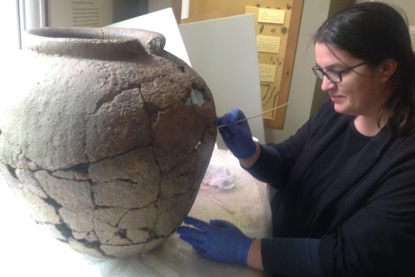 Conservator cleaning the large pottery vessel that held the Cunetion hoard.