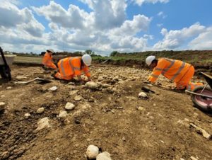 Three archaeologists in high-viz excavating a site