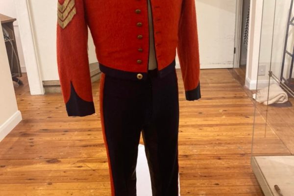 Military uniform of red jacket and black trousers with gold braid Sergeant's stripes.