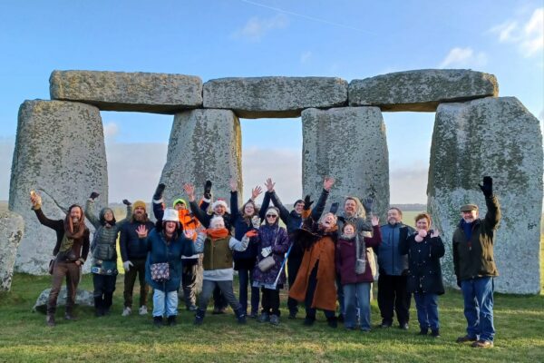 Group of 20 people waving at the camera in front of Stonehenge