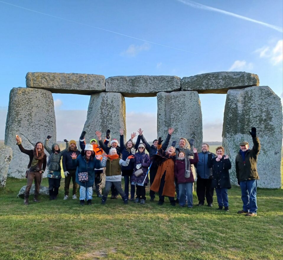 Group of 20 people waving at the camera in front of Stonehenge