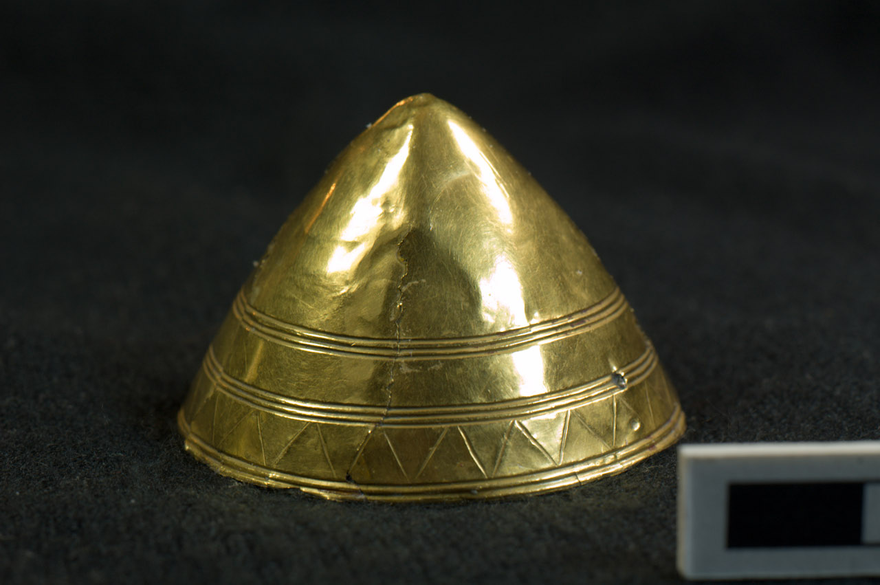 Gold cone-shaped cover for a shale button. Decorated with three bands of incised grooves, with zig-zag decoration between the two bands at the base