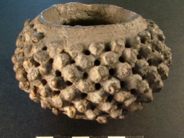 Globular pottery vessel with narrow mouth. The sides are set with eight rows of small bosses, with perforations between them.