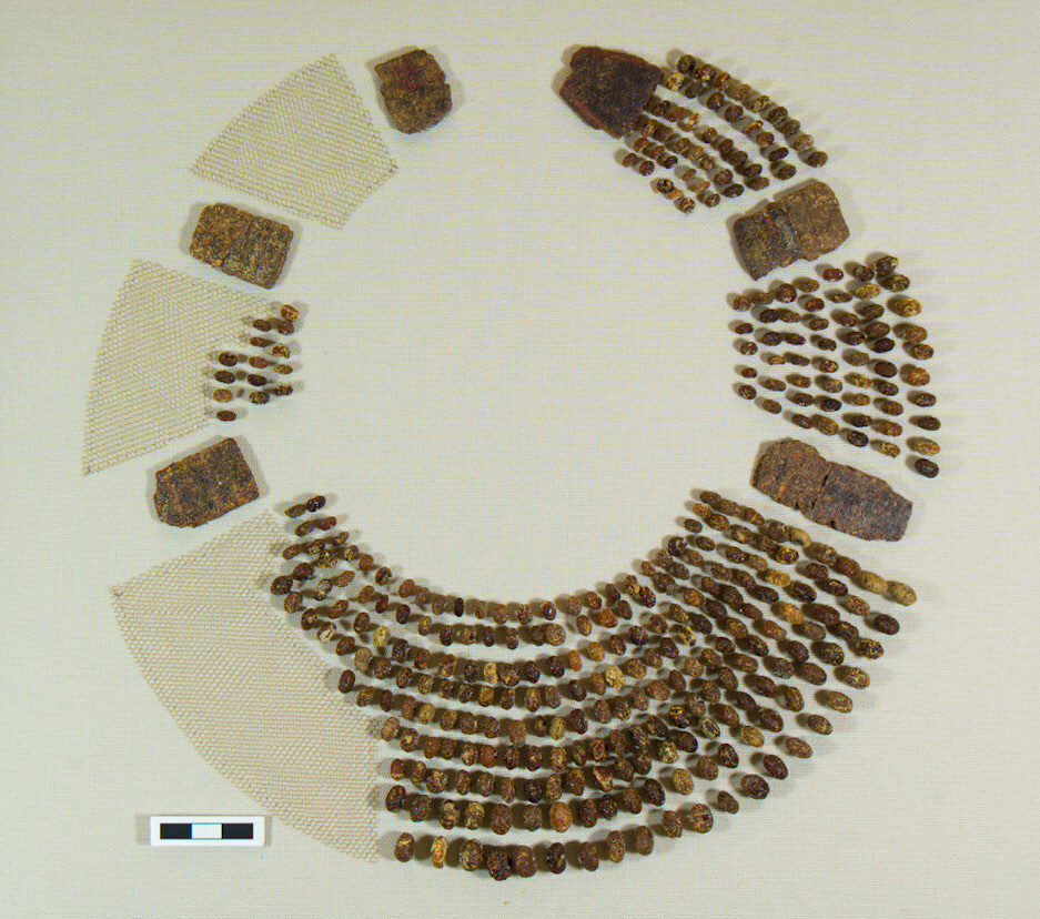 Amber necklace, with beads strung in nine rows, each row held by a rectangular spacer plate. Mounted in a museum display with approximately two-thirds of the beads in the display.