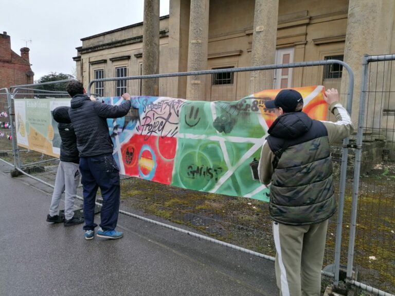 3 yong people hanging a colourful banner onto a metal railing