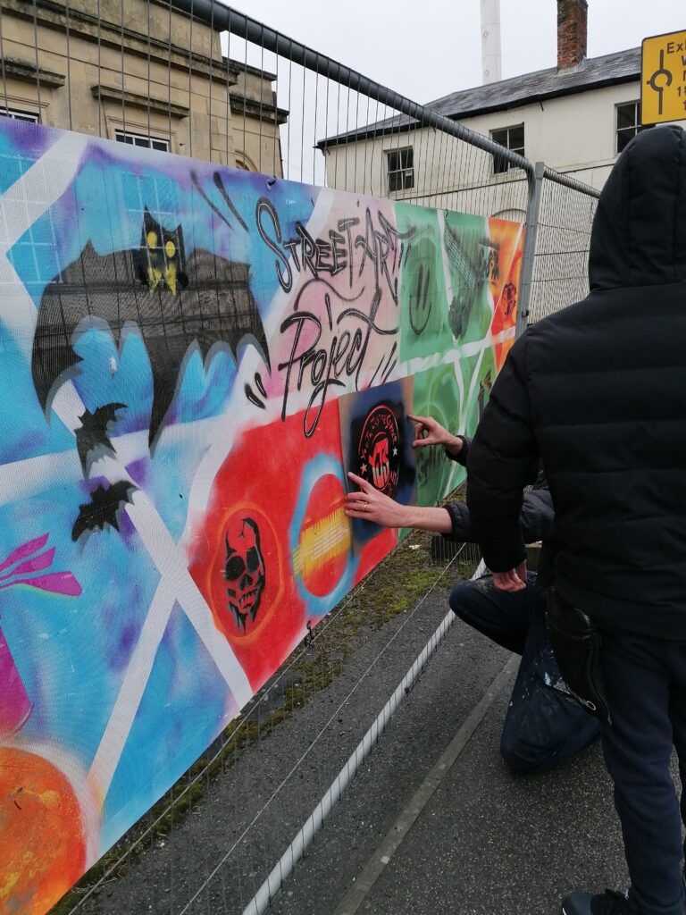 Two young people fixing a colourful graffiti banner to a metal railing